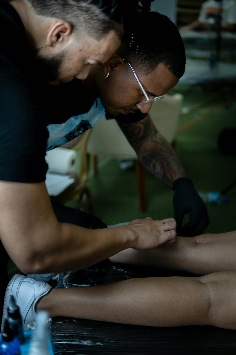 Un tatuatore lavora con cura a un disegno sulla gamba di un cliente.
