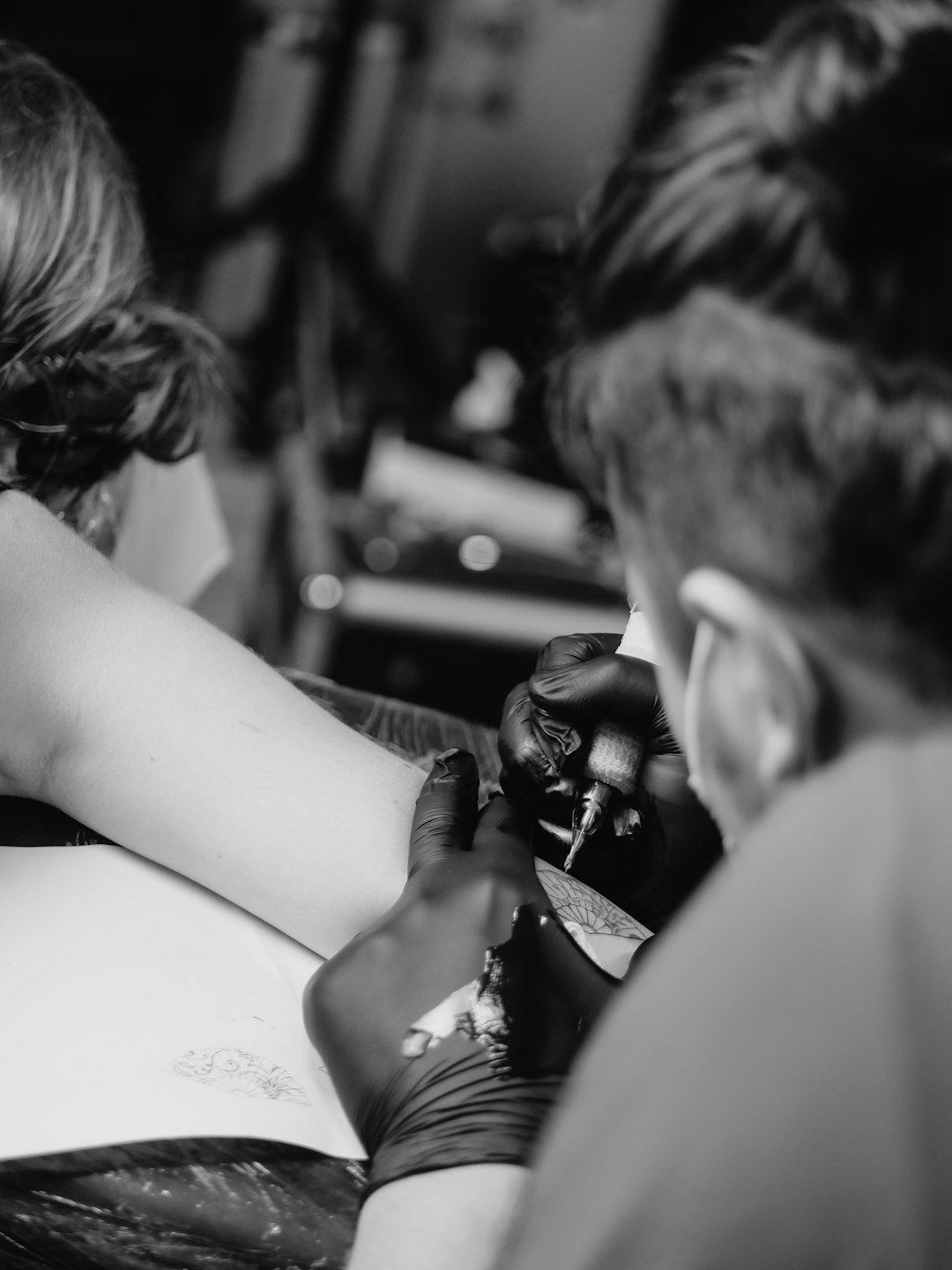 Tatuatore al lavoro sull'avambraccio di un cliente in studio.