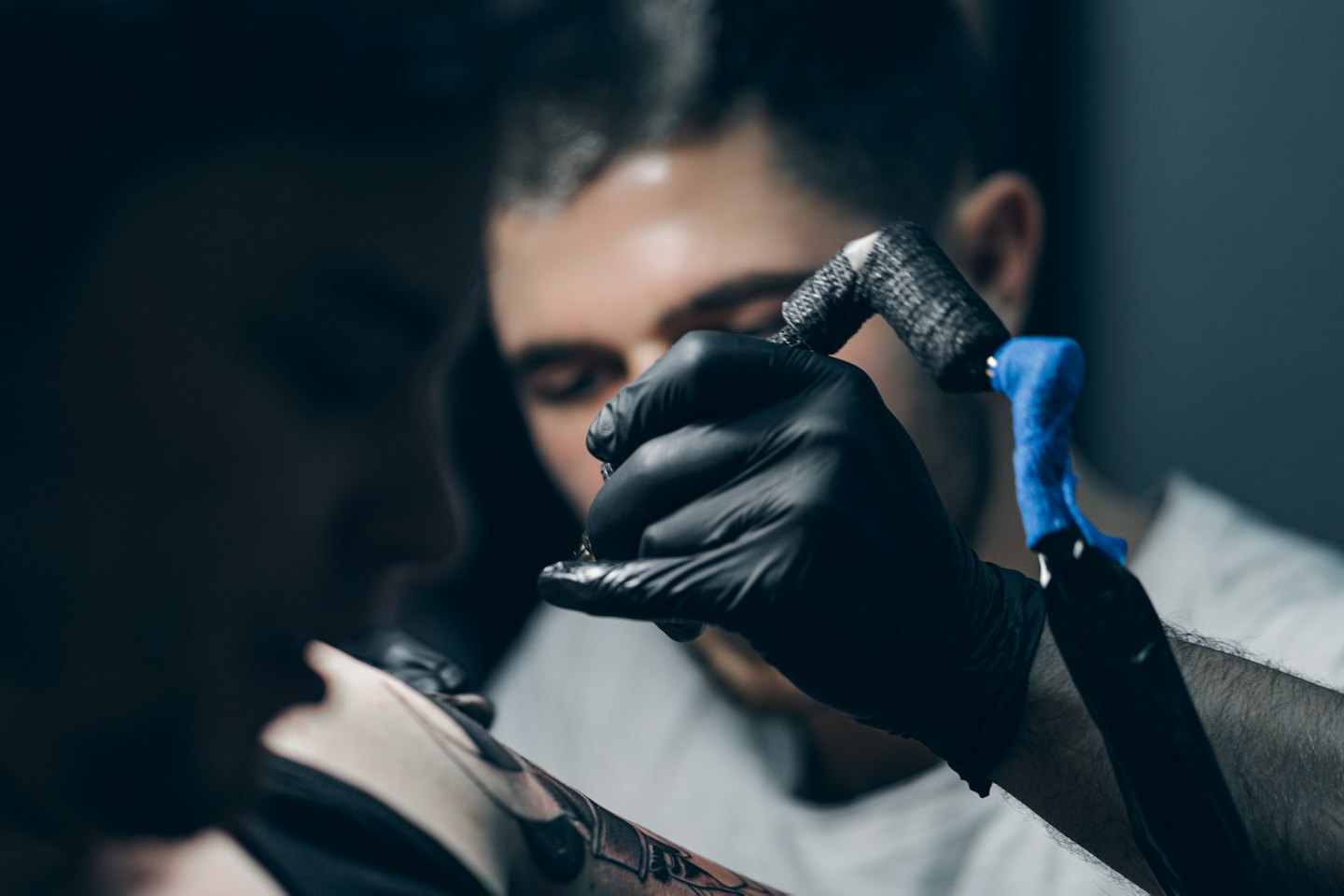 Un tatuatore tatua il braccio di un cliente con una macchinetta.