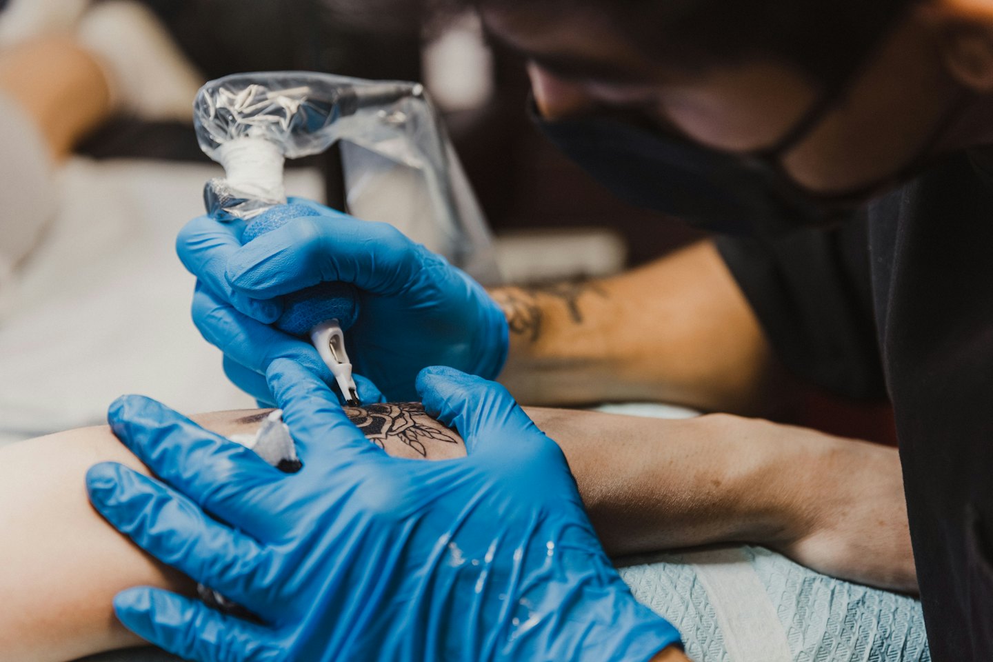 Un tatuatore applica un dettagliato inchiostro nero sull'avambraccio di un cliente.